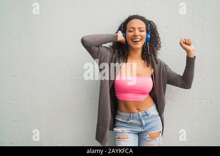 Portrait de la jeune afro-femme appréciant et écoutant de la musique avec un casque bleu. Technologie et concept de style de vie. Banque D'Images