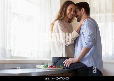 Affectueux heureux newlyweds cuddle cuisine dans la cuisine à la maison Banque D'Images