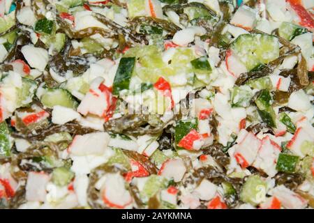 Salade de bâtonnets de crabe, d'algues, de concombre vert frais, d'œufs de poulet et de légumes verts, vêtus de mayonnaise. Vue rapprochée. Mise au point douce sélective. Banque D'Images