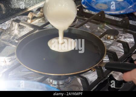 La femme verse la pâte sur une poêle chaude. Le processus de fabrication de crêpes maison. Banque D'Images