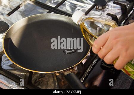 Une femme verse de l'huile végétale sur une poêle à frire chaude. Le processus de fabrication de crêpes maison. Banque D'Images