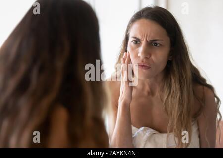 La jeune femme anxieuse regarde dans le miroir s'inquiète des problèmes de peau Banque D'Images