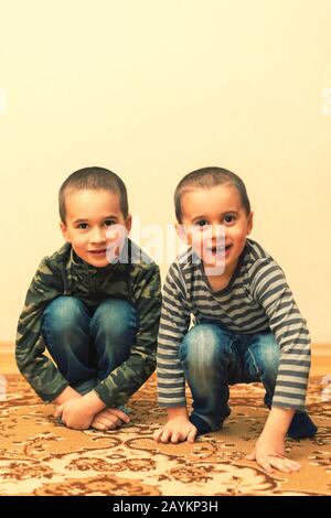 Enfants heureux assis à la maison, à l'intérieur. Deux garçons jouent dans la maison. Enfants frères jouant ensemble à la maison. Photo verticale. Tonifiée. Banque D'Images