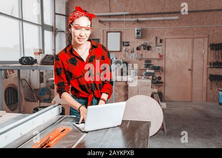 Une femme équipée d'un ordinateur portable est équipée de machines industrielles logicielles spéciales avec commande numérique en atelier ou en usine Banque D'Images