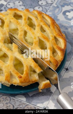 Tarte aux pommes Bramley avec garniture de pâte de treillis coupée en tranches avec un couteau à gâteau sur une plaque bleue. Arrière-plan en mosaïque bleue Banque D'Images