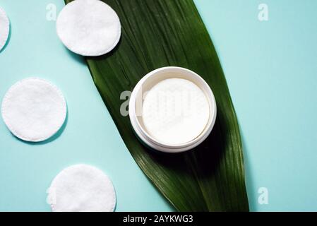 Bol avec tampons en coton liquide pour nettoyer la peau sur une feuille de palmier. Nettoyage des tampons en coton sur fond bleu pastel. CopySpace, planéité. Banque D'Images