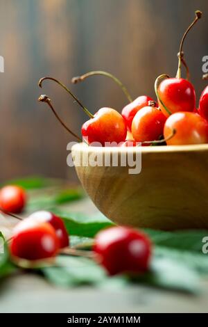 cerises douces mûres dans une plaque en bois sur un fond en bois simple. à proximité sont les feuilles. endroit pour le texte Banque D'Images