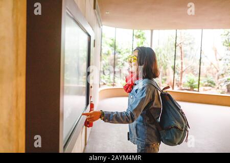 La femme utilise un écran tactile moderne interactif dans le musée zoologique du jardin ou juste un zoo. Banque D'Images