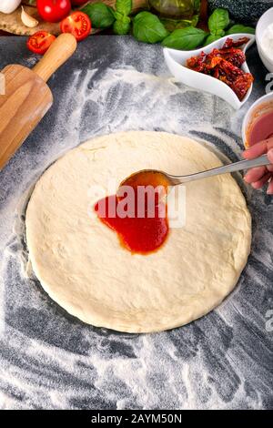 Étalage de la sauce tomate sur la pâte à pizza et bouchage pour la cuisson avec d'autres ingrédients Banque D'Images
