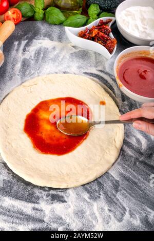 Étalage de la sauce tomate sur la pâte à pizza et bouchage pour la cuisson avec d'autres ingrédients Banque D'Images
