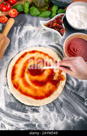 Étalage de la sauce tomate sur la pâte à pizza et bouchage pour la cuisson avec d'autres ingrédients Banque D'Images