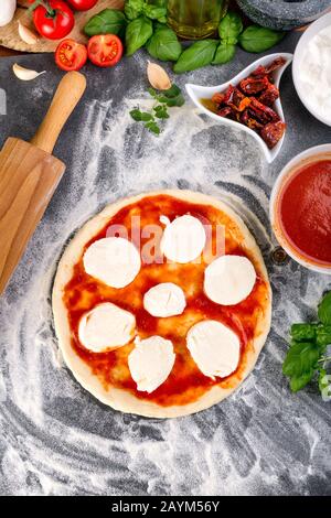 Étalage de la sauce tomate sur la pâte à pizza et bouchage pour la cuisson avec d'autres ingrédients Banque D'Images