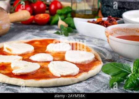 Étalage de la sauce tomate sur la pâte à pizza et bouchage pour la cuisson avec d'autres ingrédients Banque D'Images