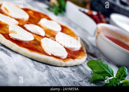 Étalage de la sauce tomate sur la pâte à pizza et bouchage pour la cuisson avec d'autres ingrédients Banque D'Images