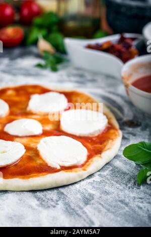 Pâte à pizza bouchées pour la cuisson avec sauce tomate, basilic et autres ingrédients. Banque D'Images