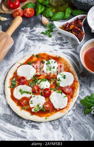 Pâte à pizza bouchées pour la cuisson avec sauce tomate, basilic et autres ingrédients. Banque D'Images