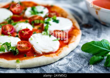 Pâte à pizza bouchées pour la cuisson avec sauce tomate, basilic et autres ingrédients. Banque D'Images