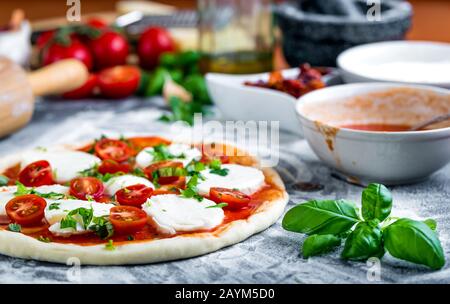 Pâte à pizza bouchées pour la cuisson avec sauce tomate, basilic et autres ingrédients. Banque D'Images