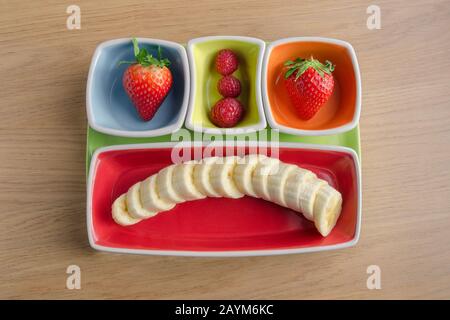 Fraises, framboises et bananes utilisées pour créer une émoticône. Dessert de fruits dans un joli plat Banque D'Images
