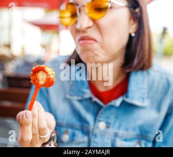 Une femme essaie de manger une saucisse gâtée, dégoûtant la nourriture rapide malsaine Banque D'Images