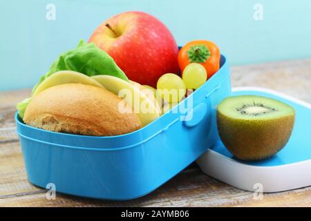 Boîte de repas saine contenant un rouleau de fromage, du poivre jaune croustillant et des fruits frais : raisins, pommes et kiwi Banque D'Images