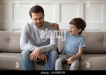 Heureux petit enfant soutenant le père bouleversé après avoir perdu le jeu vidéo. Banque D'Images