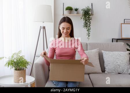 Heureux jeune femme grand public paquet d'ouverture à la maison Banque D'Images