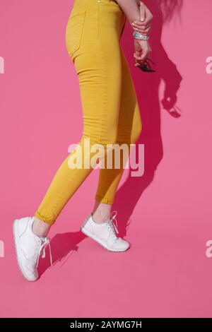 Les pieds en jaune à la mode des jeans et baskets blanches sur fond rose. Banque D'Images