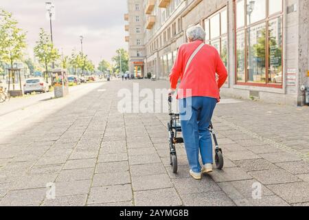 Une vieille femme âgée de haut niveau marchant seule avec un marcheur dans la rue de la ville, un concept de personnes âgées et d'invalidité Banque D'Images