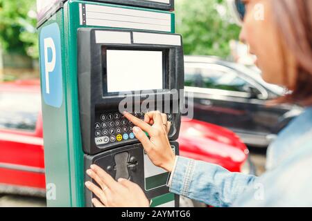 Jeune femme payant pour le stationnement en utilisant le terminal dans la rue Banque D'Images