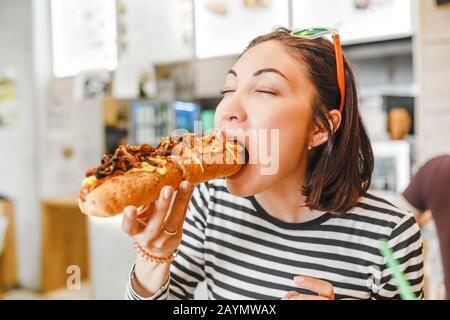 Une jeune fille qui mange un grand hot-dog dans le restaurant fastfood Banque D'Images