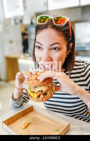 Femme mangeant un hamburger dans un café moderne fastfood, concept de déjeuner Banque D'Images