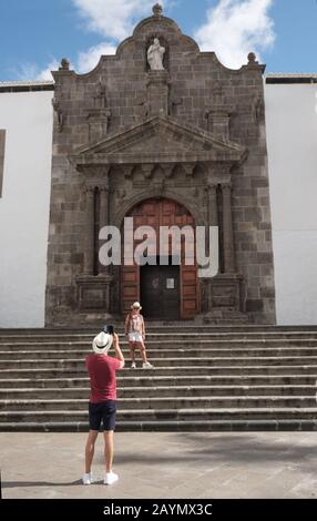 Homme de tourisme en chapeau et short prenant photo de femme au téléphone par grande porte, Plaza San Francisco, Santa Cruz de la Palma, îles Canaries, Espagne Banque D'Images