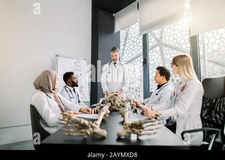 Jeunes étudiants en médecine multiethnique sur la leçon d'anatomie dans la salle de classe moderne. Professeur de médecin d'âge moyen enseignant l'anatomie à l'aide du squelette humain Banque D'Images