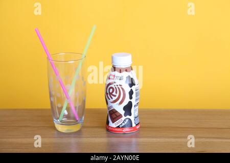 Une bouteille de lait au chocolat Muller Frijj à côté d'un verre à pois demi-pinte avec deux pailles sur table en bois avec espace publicitaire sur fond jaune Banque D'Images