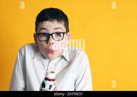 Un jeune garçon de 8 ans boit une bouteille de lait au chocolat Muller Frijj sur fond jaune Banque D'Images