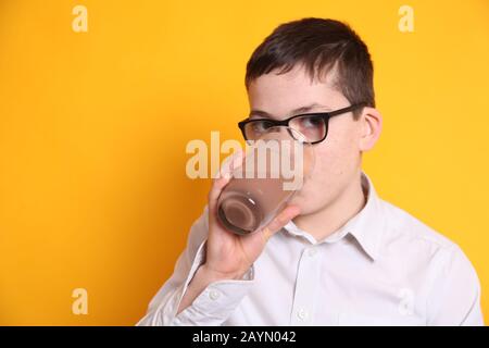Un jeune garçon de 8 ans boit un verre de lait au chocolat sur fond jaune Banque D'Images