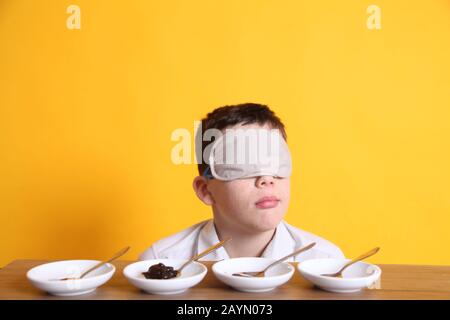 Test de goût à l'aveugle, jeune garçon de 12 assis avec des plats d'échantillon de nourriture pour goûter différentes denrées alimentaires bandés Banque D'Images