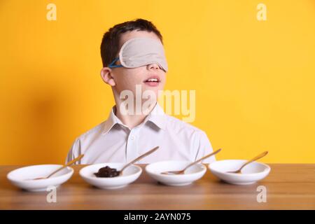 Test de goût à l'aveugle, jeune garçon de 12 assis avec des plats d'échantillon de nourriture pour goûter différentes denrées alimentaires bandés Banque D'Images