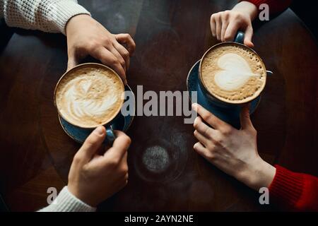 Image de dessus de l'homme et de la femme tenant des tasses de café chaudes assis à table en bois, photo courte. Romance, date romantique, amour, sentiment et émotio Banque D'Images