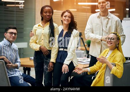 Un groupe d'adultes heureux et réussis portant des vêtements décontractés et se tenant les uns les autres au bureau, se posant à l'appareil photo. Vos collègues préférés Banque D'Images