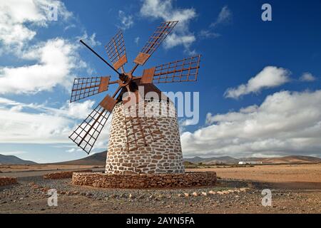 Moulin à vent traditionnel à Tefia, Fuerteventura. Voiles en bois et toit, bâtiment en pierre ronde blanchi à la chaux. Ciel bleu et nuages. Paysage volcanique. Banque D'Images