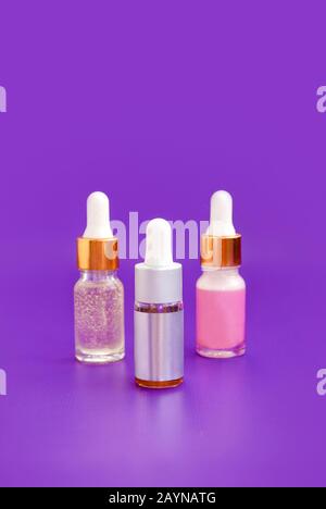 Trois bouteilles d'huile cosmétique, sérum de soin de la peau sur un fond violet. Placer pour le texte Banque D'Images