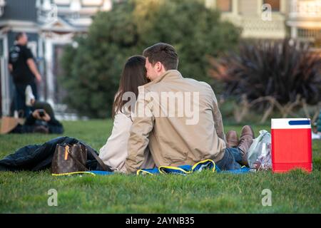 Un couple flirte sur l'herbe à Alamo Square par les dames Peintes à San Francisco. Banque D'Images