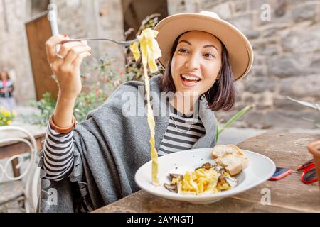 Une heureuse femme asiatique mangeant des pâtes avec truffe dans le restaurant italien extérieur Banque D'Images