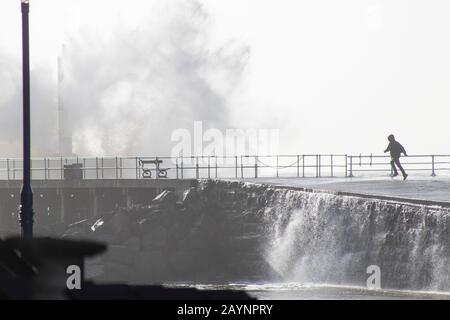 L'homme traverse des vagues pendant la tempête Dennis à Aberystwyth, au Pays de Galles. Banque D'Images