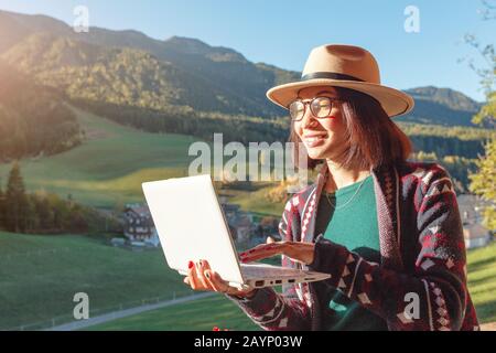 Heureuse jeune femme freelance travaillant à distance à l'aide d'un ordinateur portable dans la maison de campagne avec Alpes montagnes à l'arrière-plan Banque D'Images