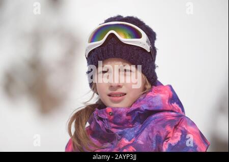 belle fille caucasienne souriante et active dans un chapeau de laine et une veste de snowboard avec des friandises de ski pendant les loisirs d'hiver en plein air recréé Banque D'Images