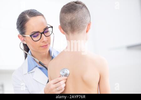 Le pédiatre de la jeune femme médecin examine le patient garçon avec stéthoscope. Banque D'Images