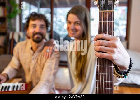 Homme et femme chamanique tenant de la guitare classique avec des cordes de nylon et homme jouant l'harmonium pour la musique sacrée et kirtan regardant l'appareil photo Banque D'Images